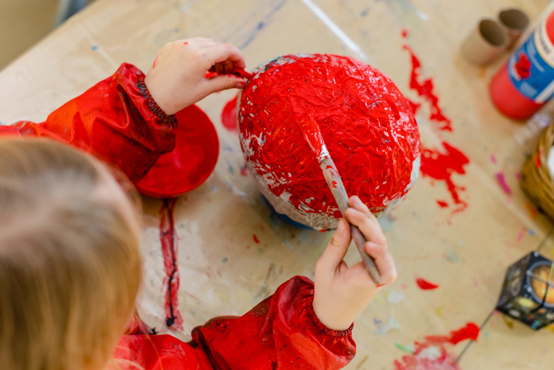 Ein Kind bemalt einen Gegenstand mit roter Farbe.