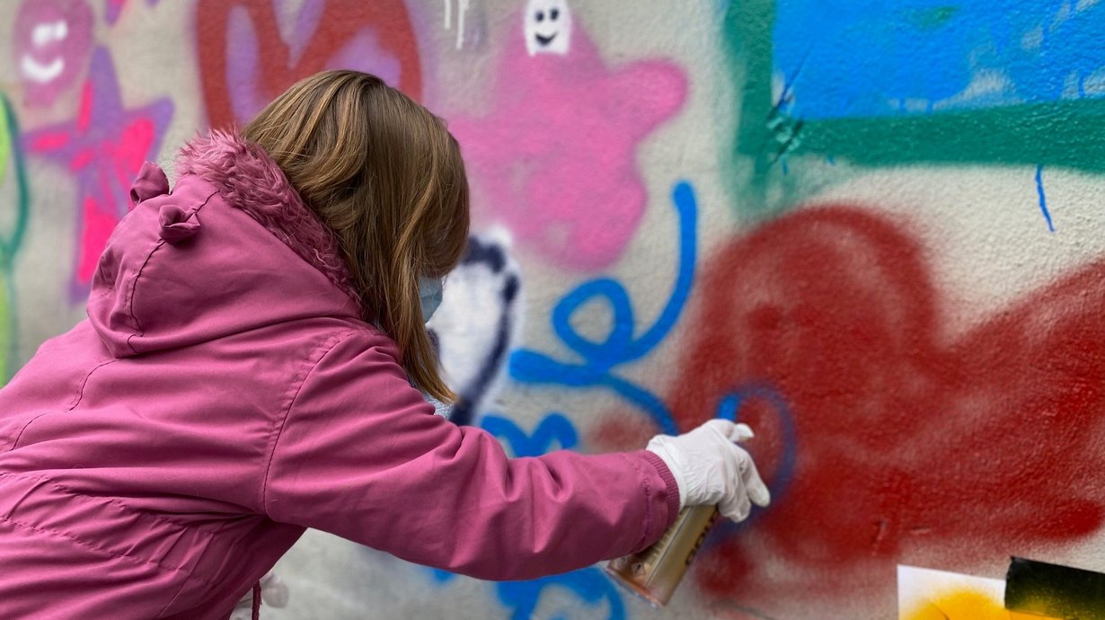Kind sprüht Farbe auf eine Wand. 