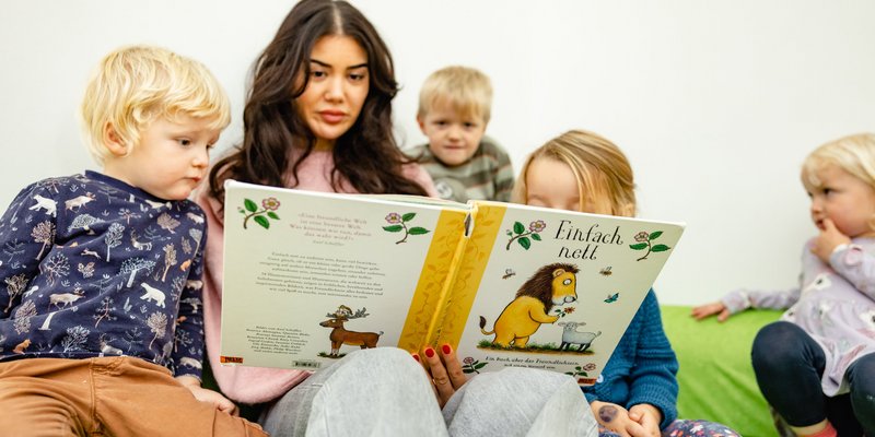 Ein älteres Kind liest vier kleinen Kindern aus einem Buch vor.